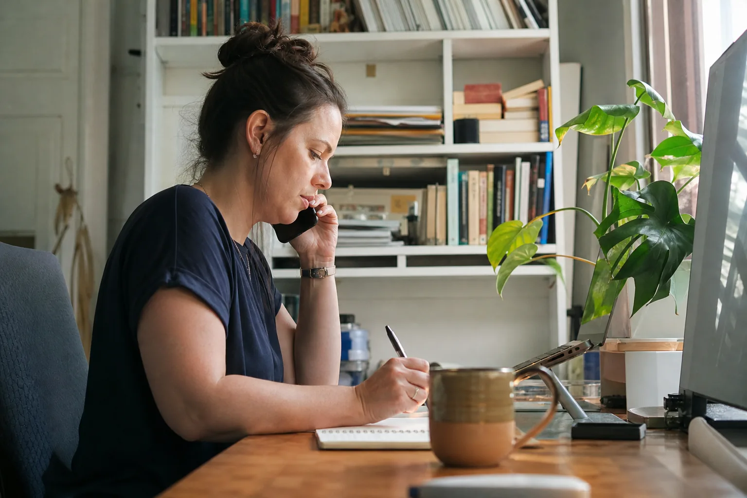 Assistant taking handwritten notes during a phone call at her home office