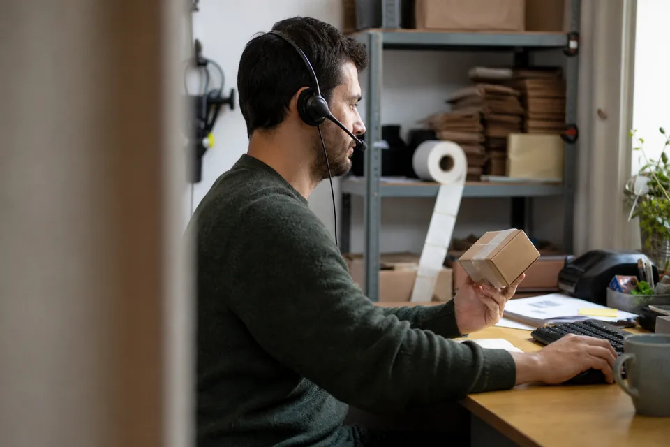 Customer service assistant with a headset answering a chat while holding a returned parcel