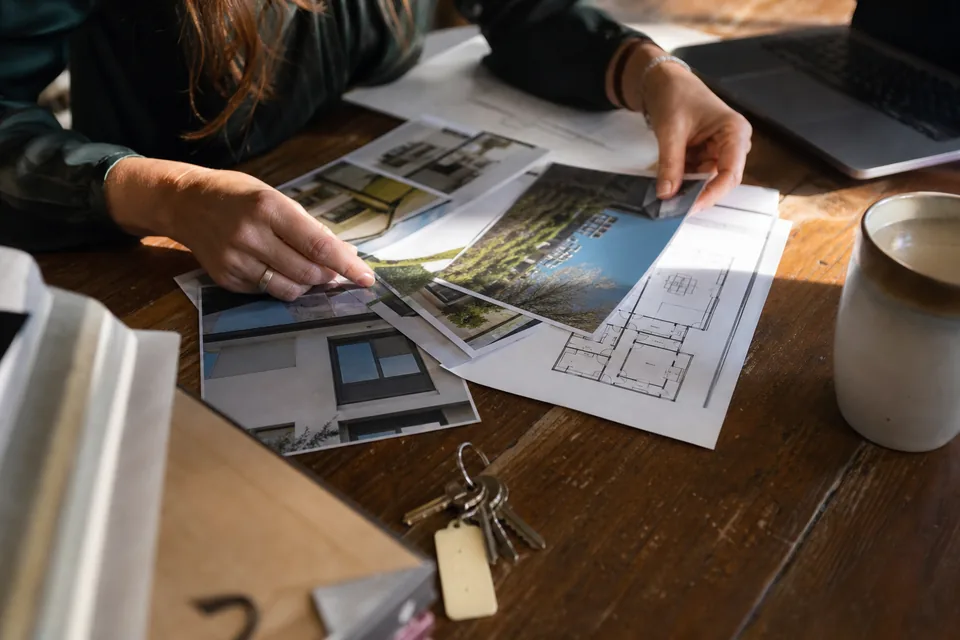 Assistant preparing a property listing with printed floor plans, house photos and keys on a desk