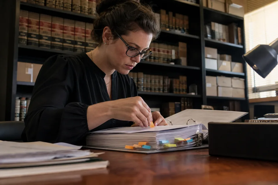 Legal assistant organizing a case binder with colored tabs at a desk with law books behind