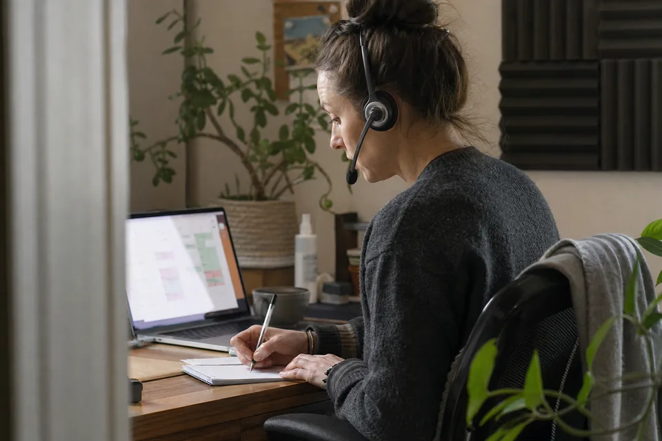 Receptionist with a headset taking a call and writing a message beside an appointment calendar